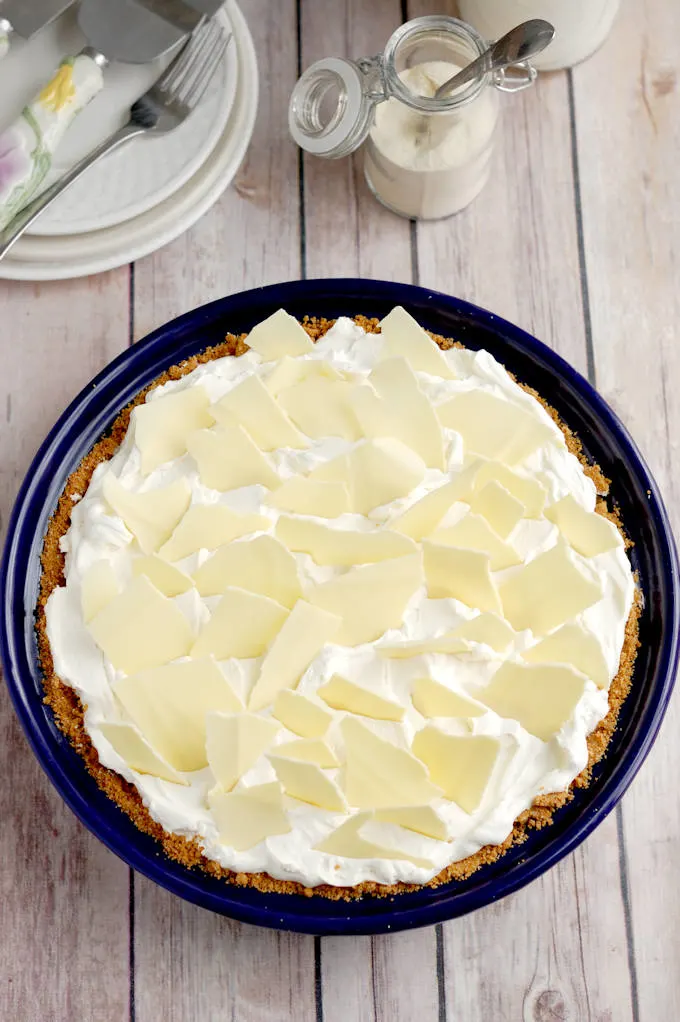 a malted milk cream pie in a blue pie plate set on a wood table.