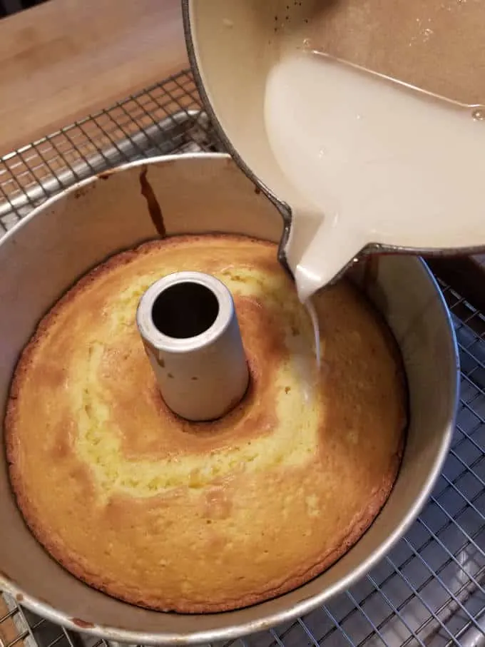 Syrup being poured over a baked cake in a pan.