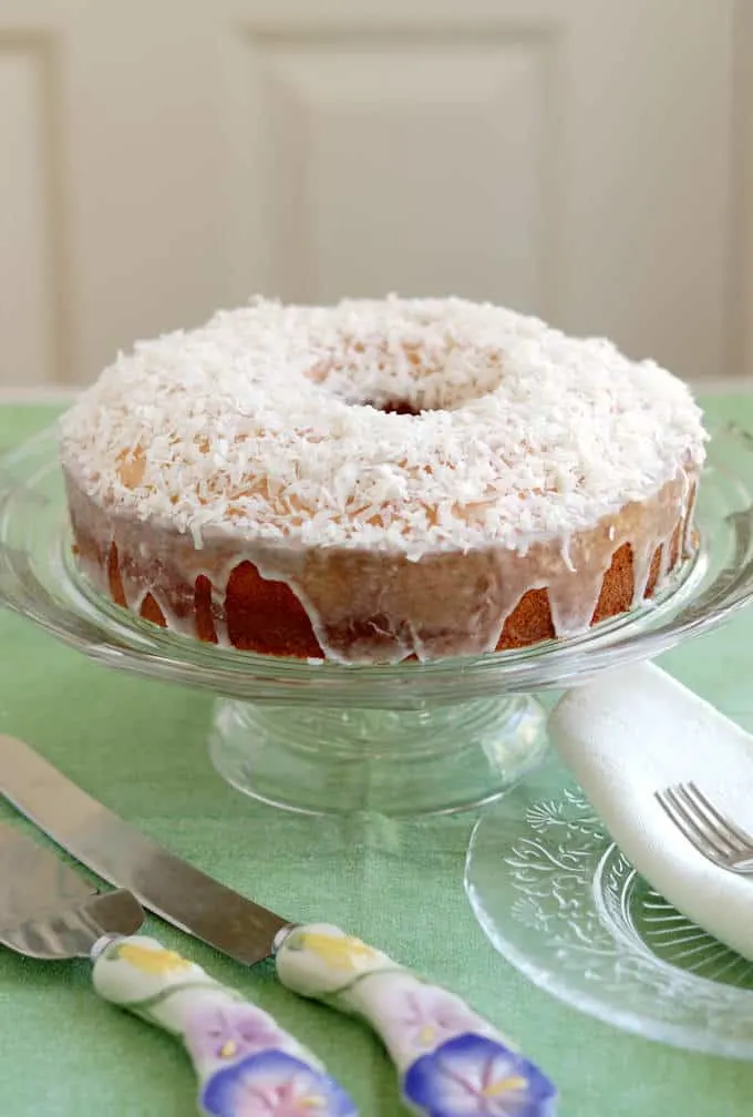 A coconut cake on a glass cake stand.