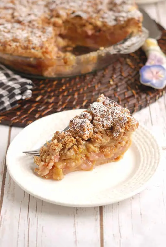 a slice of rhubarb crumb pie on a white plate. Pie pan in background.