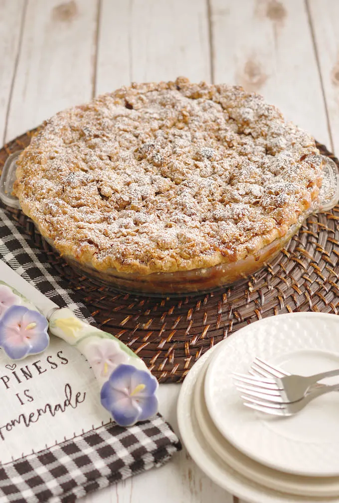 a freshly baked rhubarb crumb pie on a table with serving dishes.