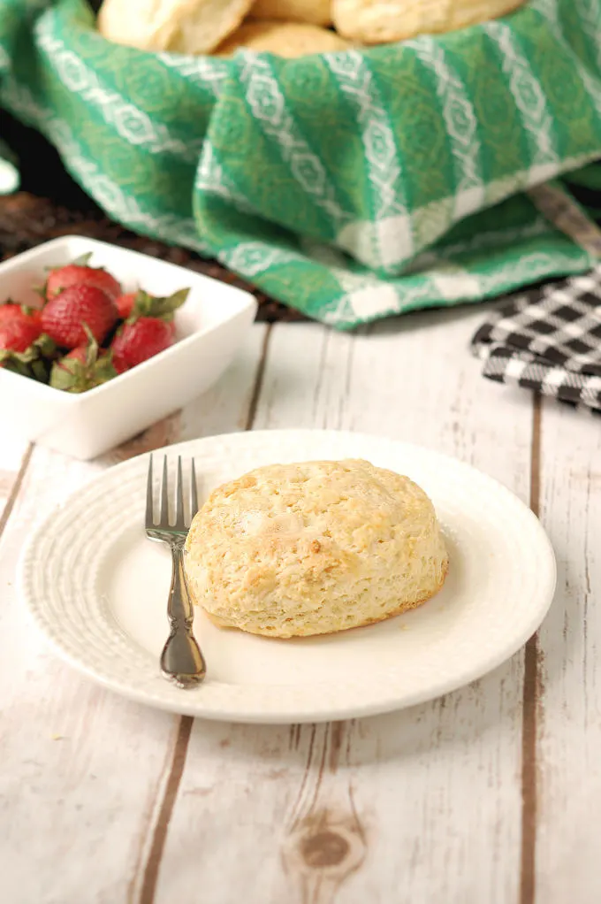 a shortcake biscuit on a white plate with a bowl of strawberries in the background.
