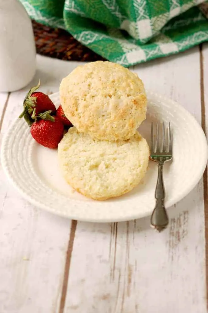 a split shortcake biscuit on a plate with three strawberries and a fork