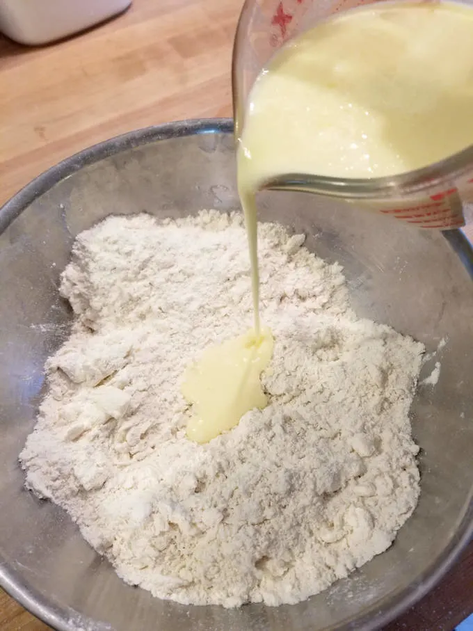 a cup pouring buttermilk into a bowl of shortcake biscuit mix