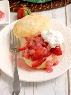 showing a shortcake with strawberries rhubarb and cream on a white plate