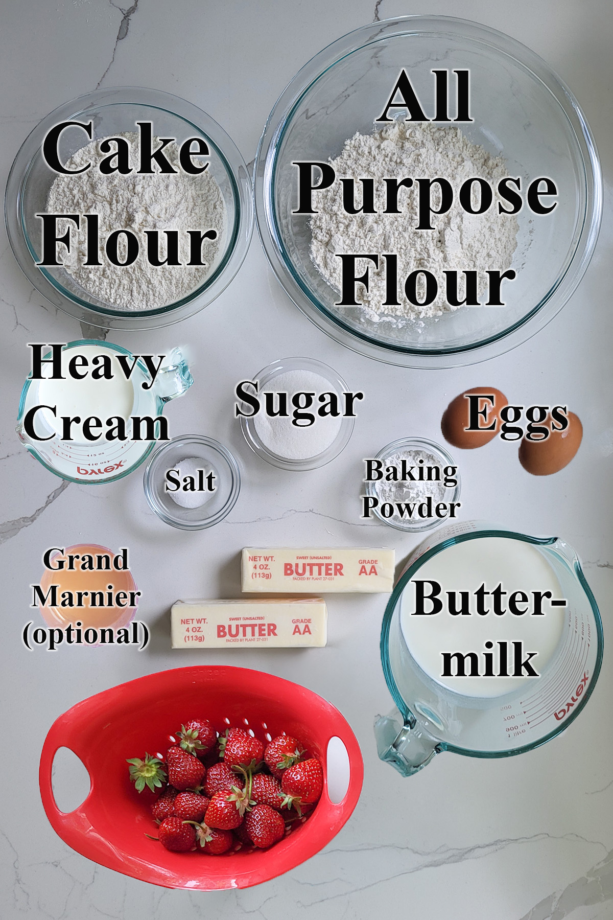 ingredients for strawberry shortcakes in glass bowls on a white surface. 