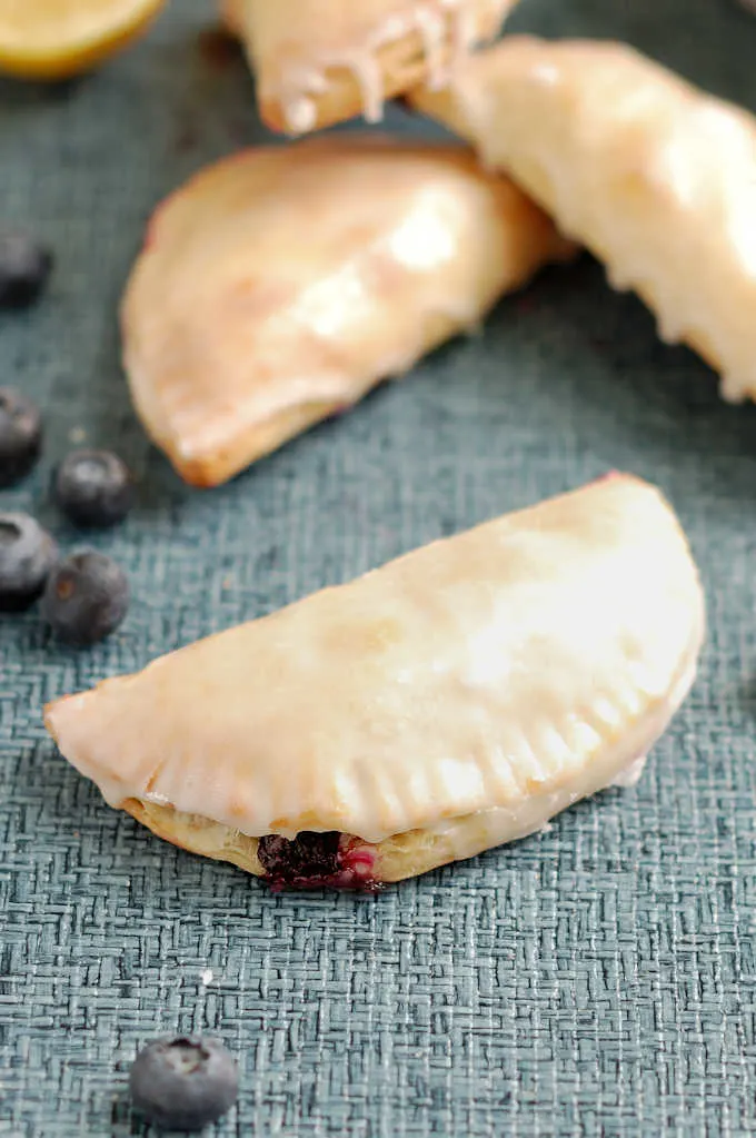 a glazed blueberry hand pie on a blue surface