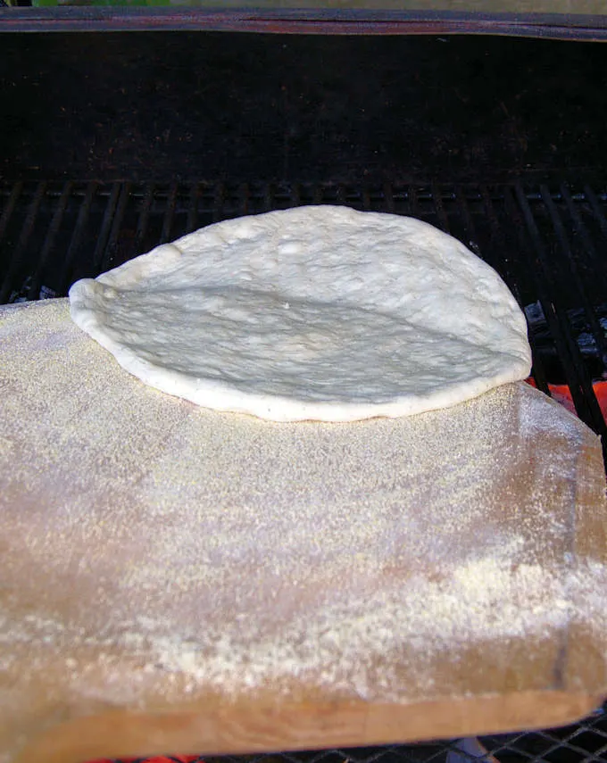 sliding pizza dough from a wooden peel onto a grill