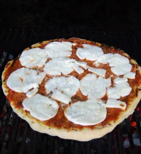 a pizza with tomato sauce and mozzarella on a grill