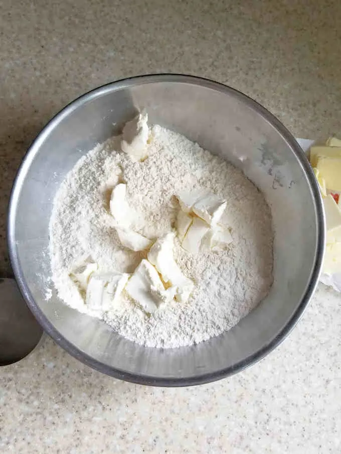 a bowl of flour with chunks of cream cheese on top