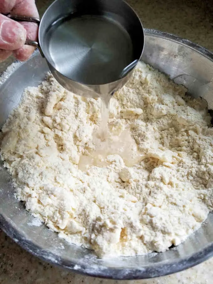a cup of water being added to pie dough
