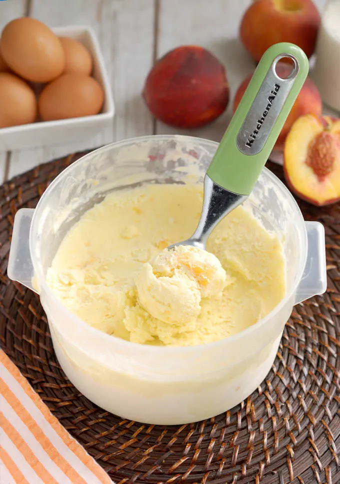 a bin of roasted peach ice cream with an ice cream scoop.