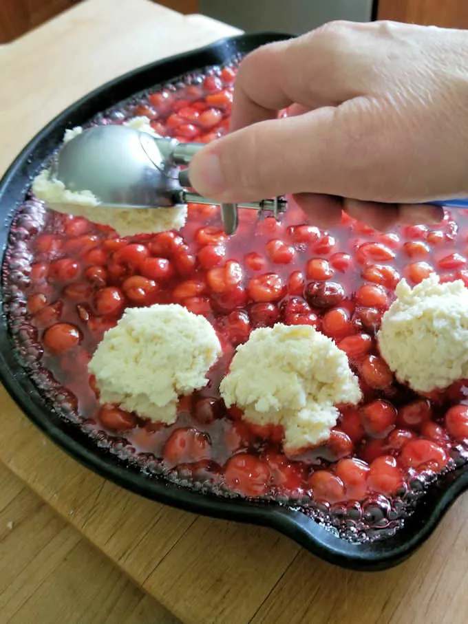 koekjesdeeg scheppen voor het toppen van sour cherry cobbler.