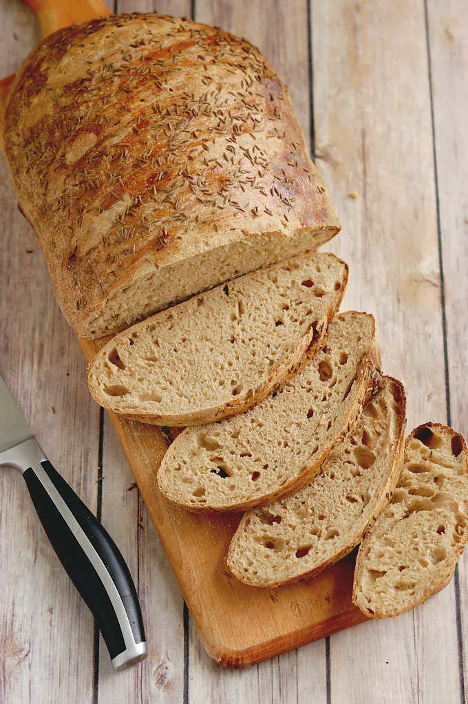 a loaf of sliced sourdough rye bread on a cutting board.
