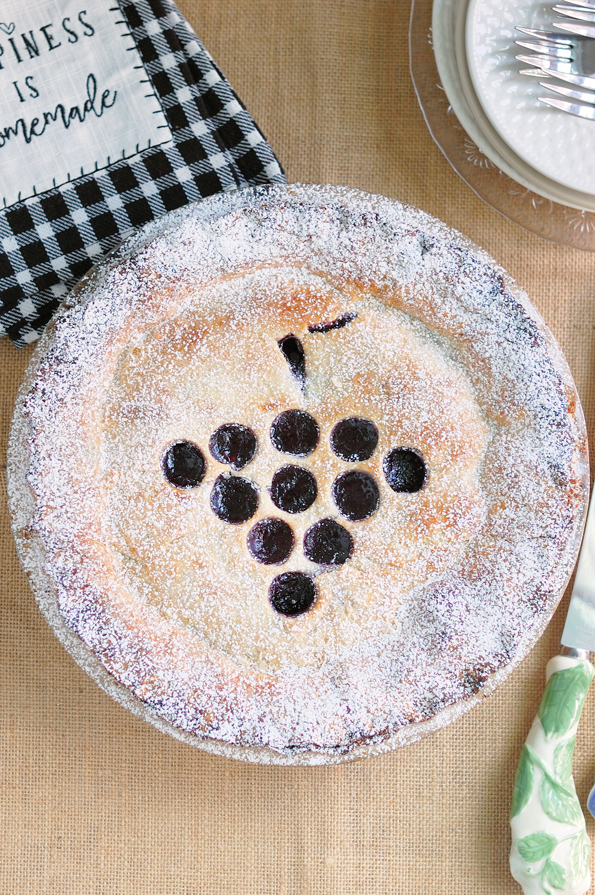 an overhead shot of a whole concord grape pie on a beige surface.