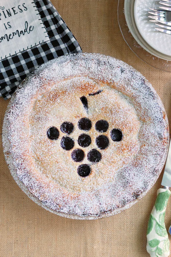 top view of a concord grape pie with sugar topping on a beige background