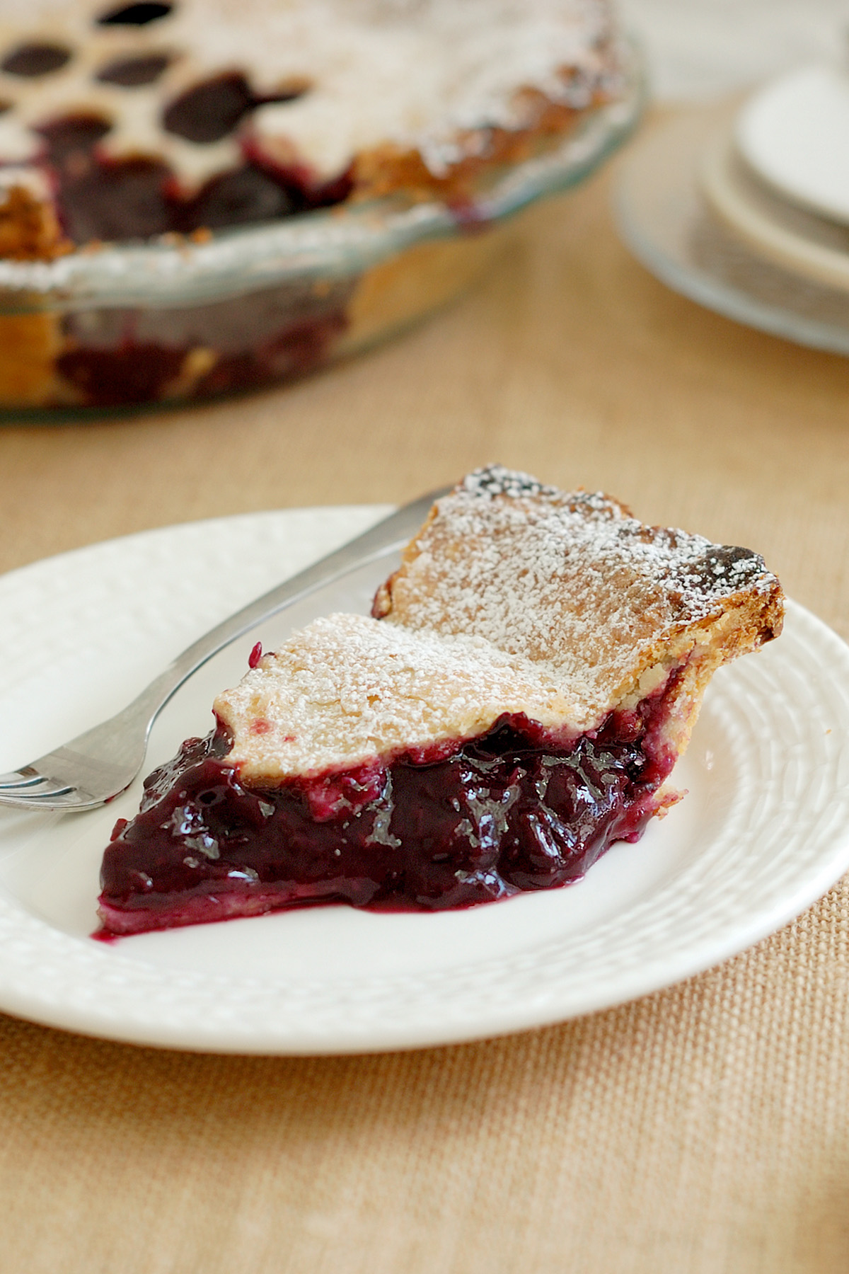 A slice of concord grape pie on a white plate with a fork.