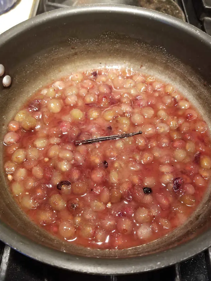 Concord grape pulp cooking in a pan with a vanilla bean