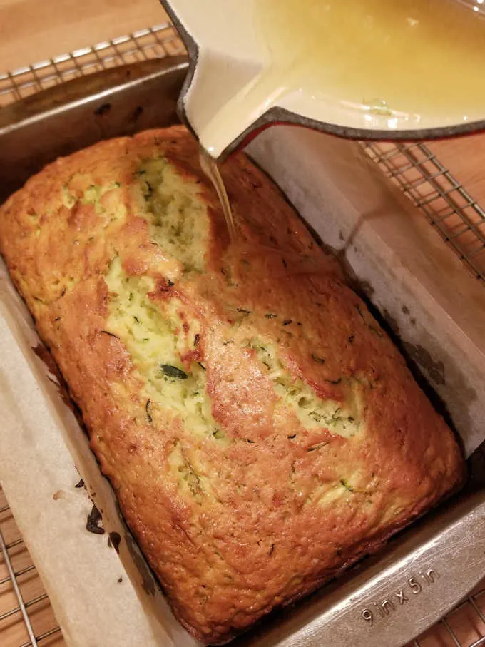 pouring lemon glaze over freshly baked zucchini bread