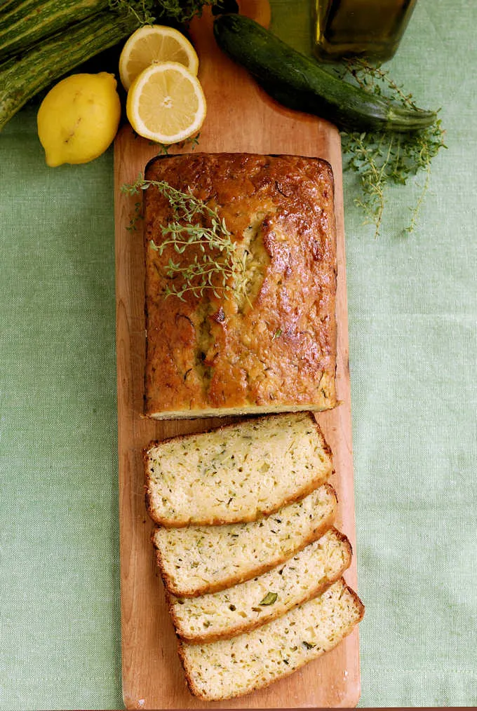 a cutting board with a sliced loaf of lemon zucchini bread with olive oil and thyme
