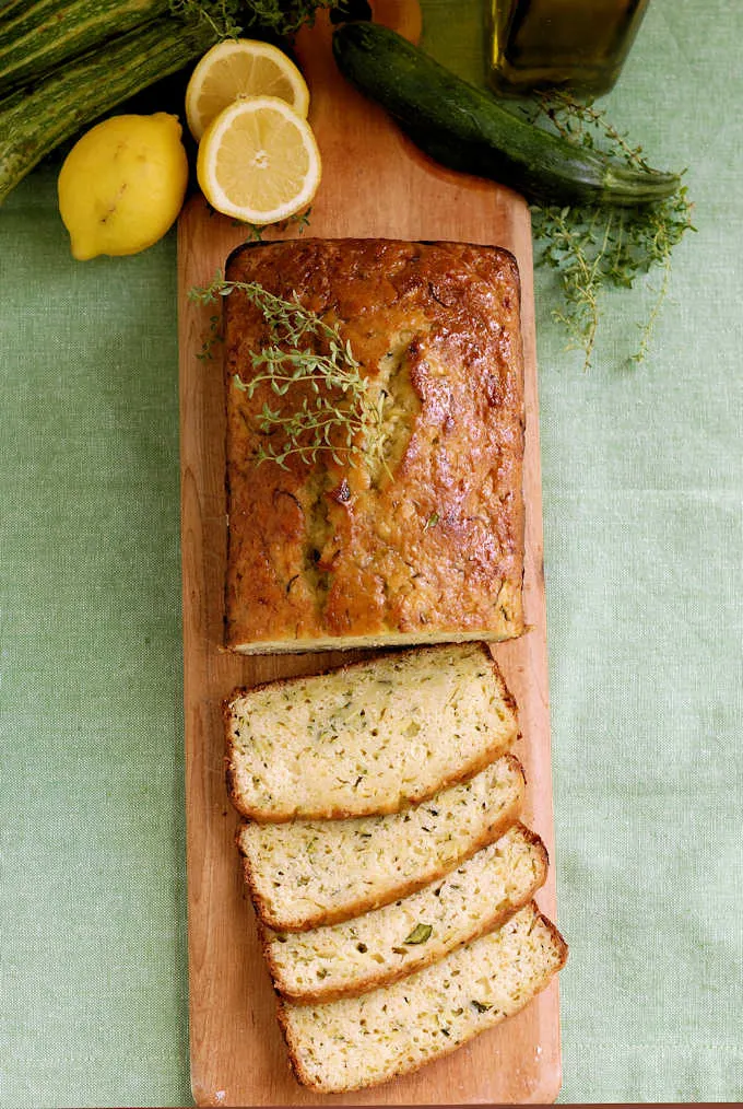 a cutting board with a sliced loaf of lemon zucchini bread with olive oil and thyme