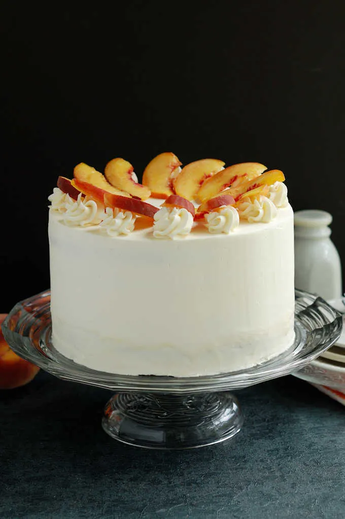 a peach melba cake on a glass cake stand against a black background