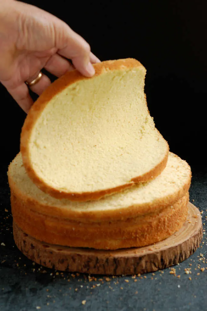 a hand bending a layer of vanilla cake