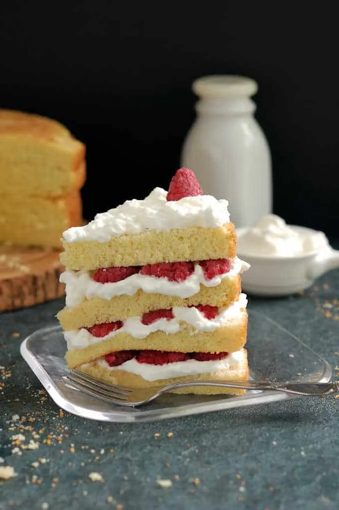 a slice of vanilla cake with raspberries and cream on a plate.