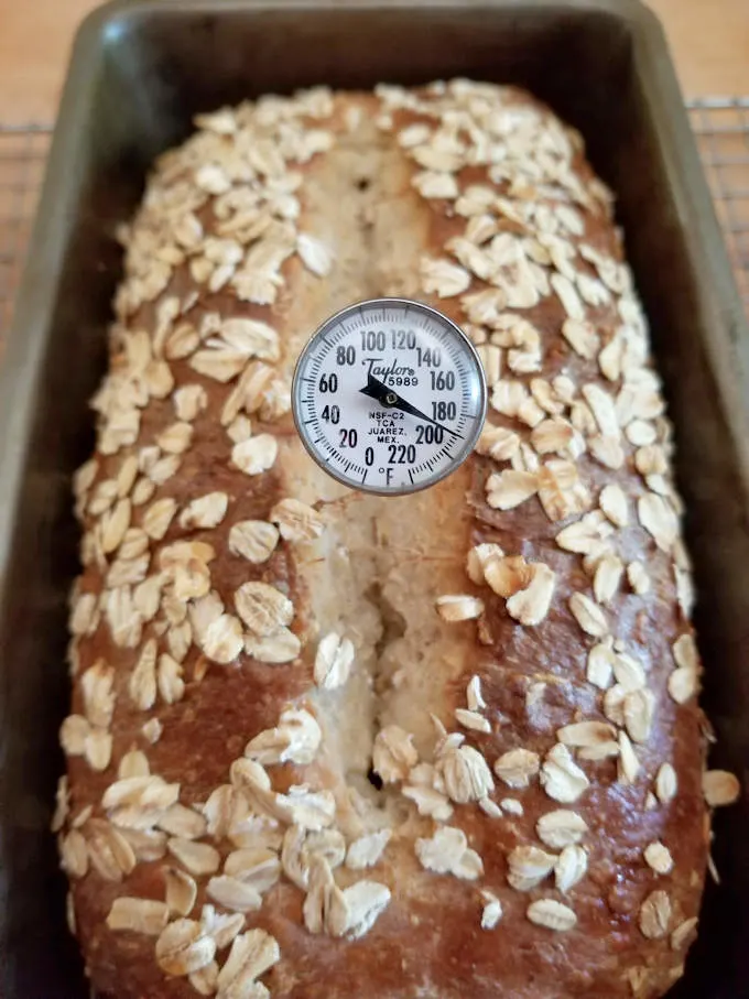 a baked loaf of honey oat bread with a thermometer at 190 degrees F.