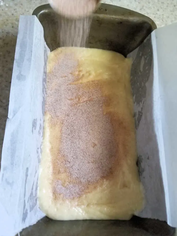 a loaf pan lined with parchment paper, filled with batter and sprinkled with cinnamon sugar