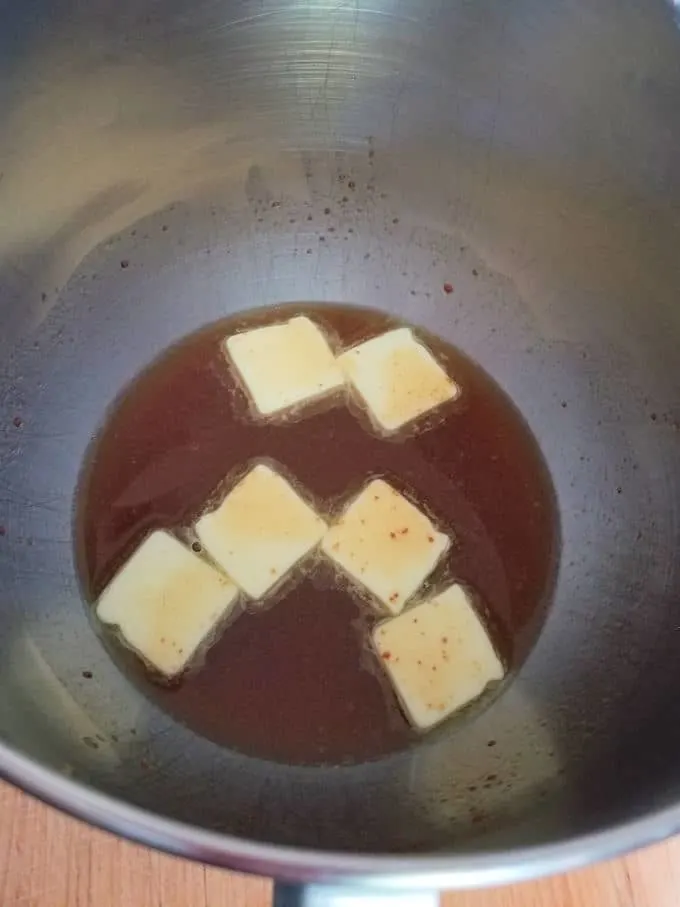 a bowl of reduced apple cider with chunks of butter melting in the warm cider