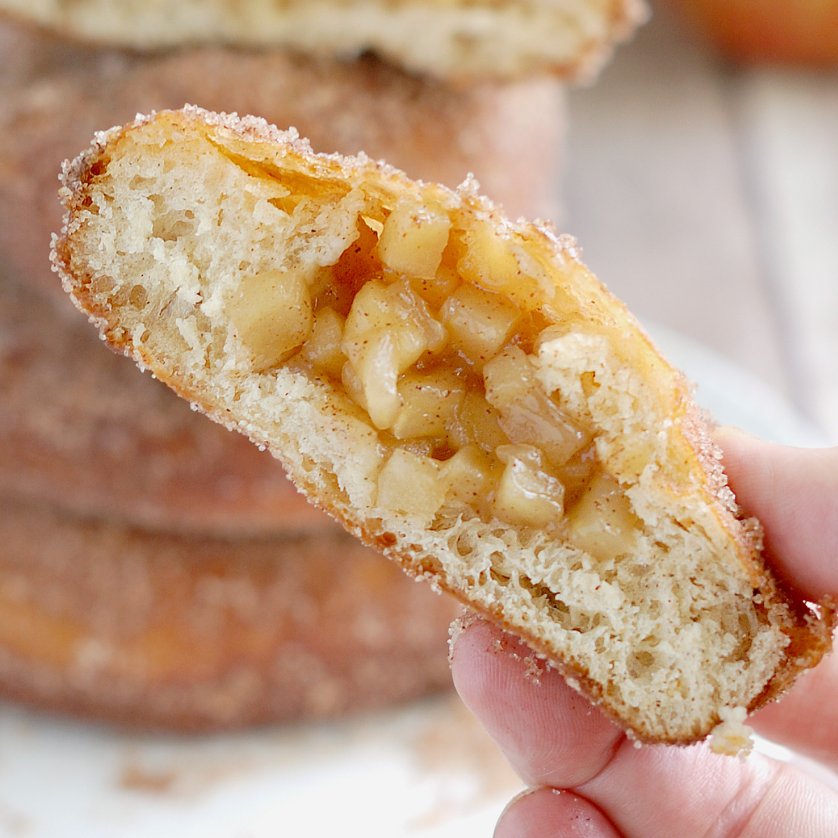 a hand holding half of an apple filled donut.