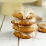 a stack of iced apple oatmeal cookies on a white surface.