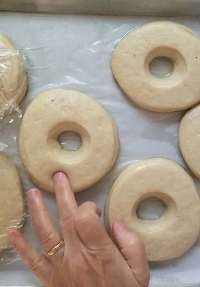 a finger poking a raw donut to check if it has risen enough
