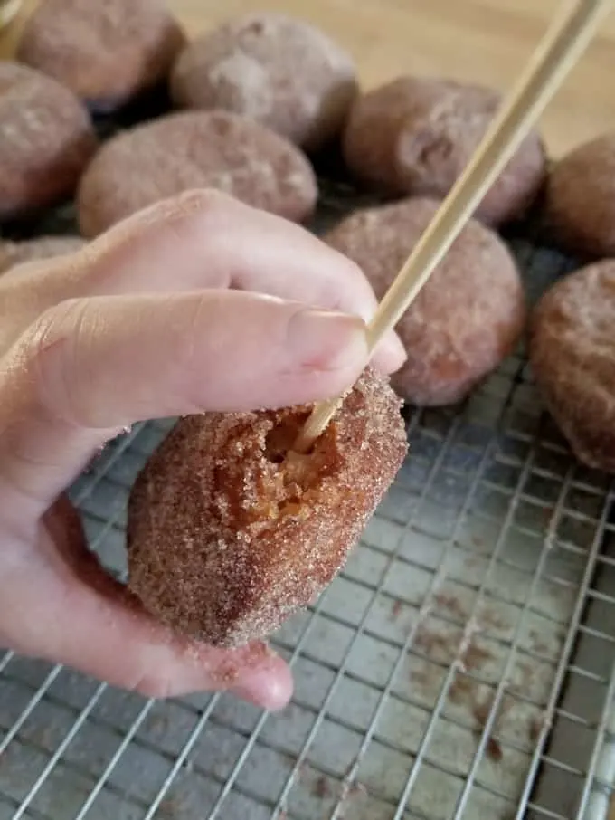 a skewer poking a hole in the end of a cider donut