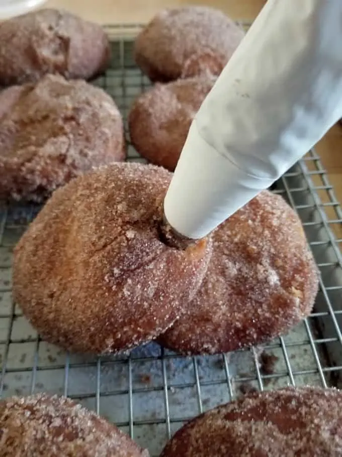 a pastry bag piping apple filling into a cider donut