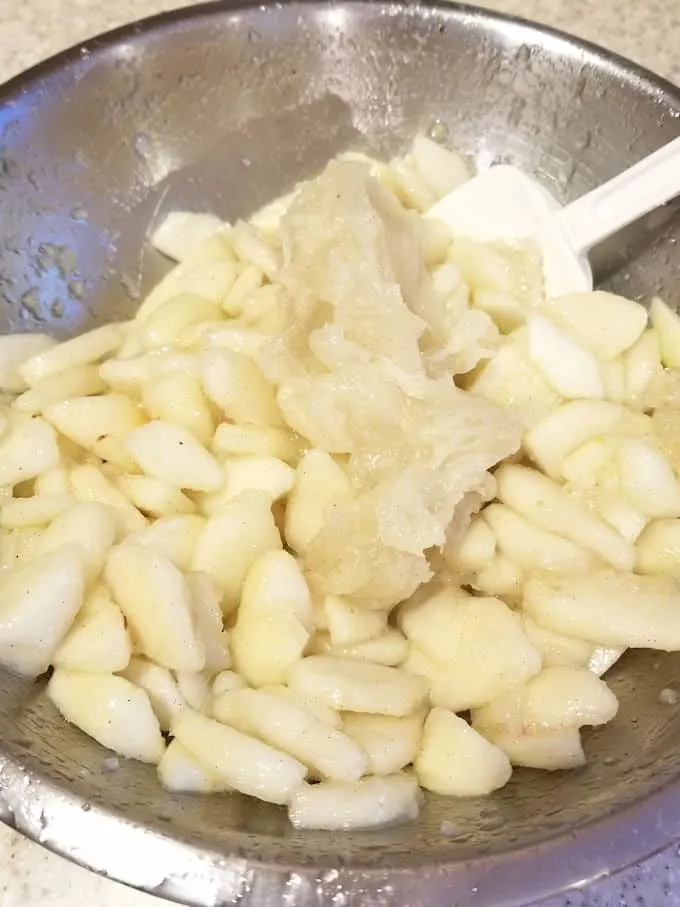a spatula mixing thickened pear juice into pear chunks to make pear pie filling