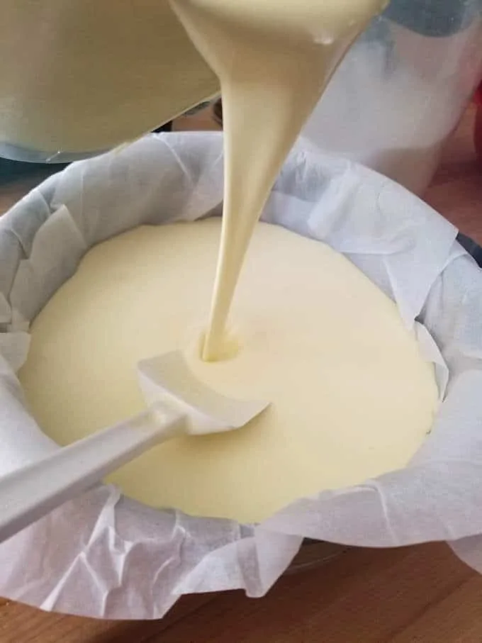 Pouring san sebastian cheesecake batter into a parchment lined spring form pan.
