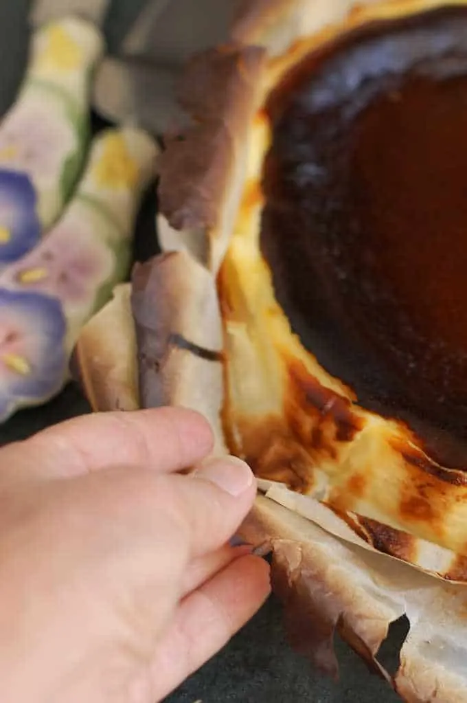 closeup of peeling parchment away from sides of san sebastian cheesecake.