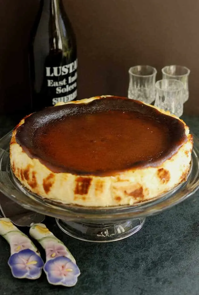 a san sebastian cheesecake on a cake stand in front of a bottle of sherry 