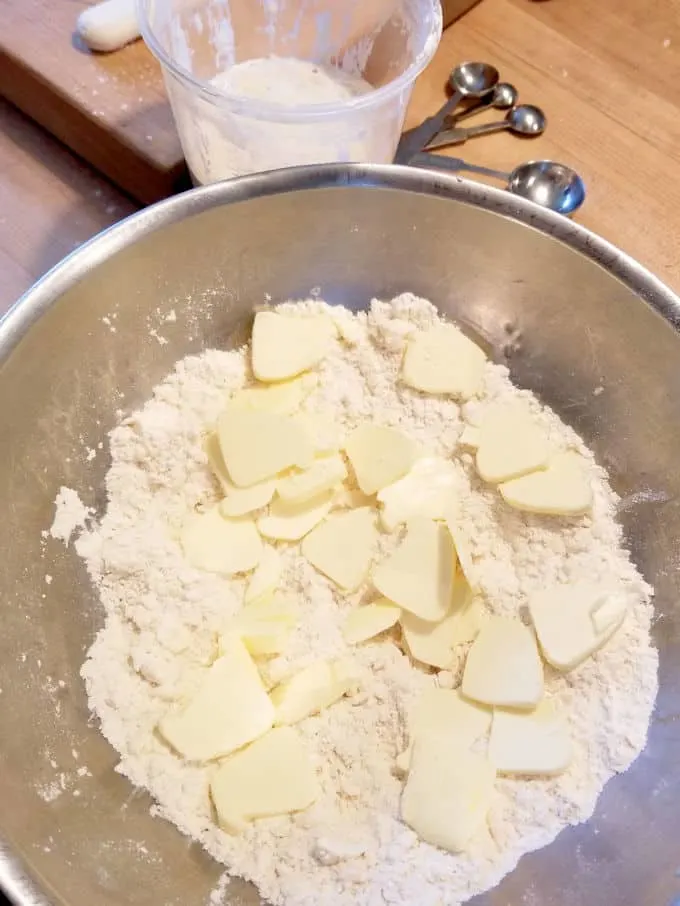 a bowl of flour with slices of butter scattered on top