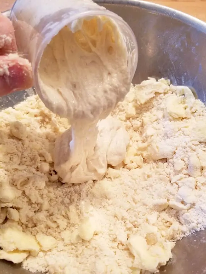 a cup of sourdough discard pouring into a bowl of pie dough mix