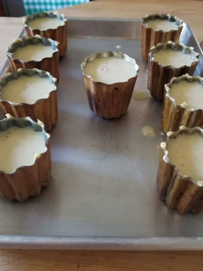 canele pans filled with batter on a baking sheet