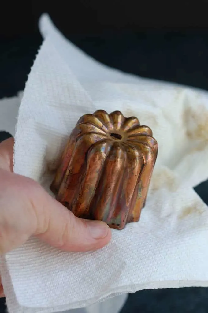 cleaning a canele mold with a paper towel
