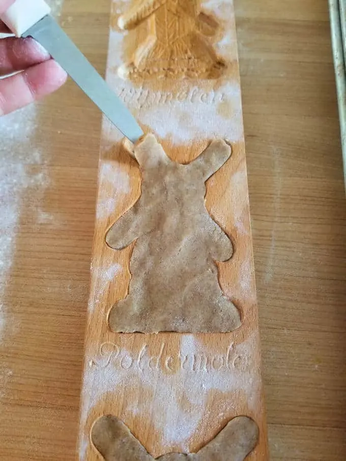 the tip of a knife loosening the edge of a speculaas cookie from a wooden mold