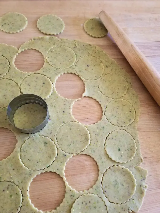 pistachio linzer dough rolled out on a wooden table, with a cookie cutter