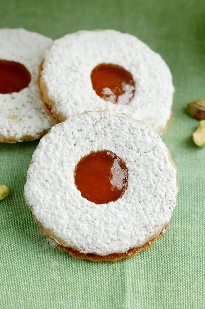 three pistachio linzer cookies on a green background