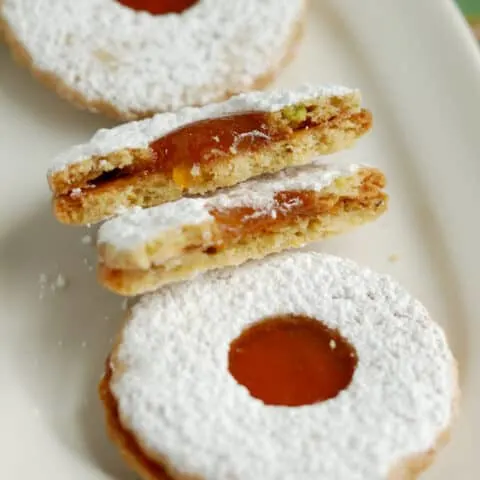 a plate with two whole and one broken pistachio linzer cookie
