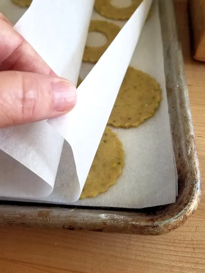 a sheet pan with layers of parchment paper and unbaked pistachio cookies ready for the freezer