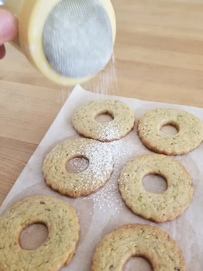 sprinkling powdered sugar onto the tops of pistachio linzer cookies